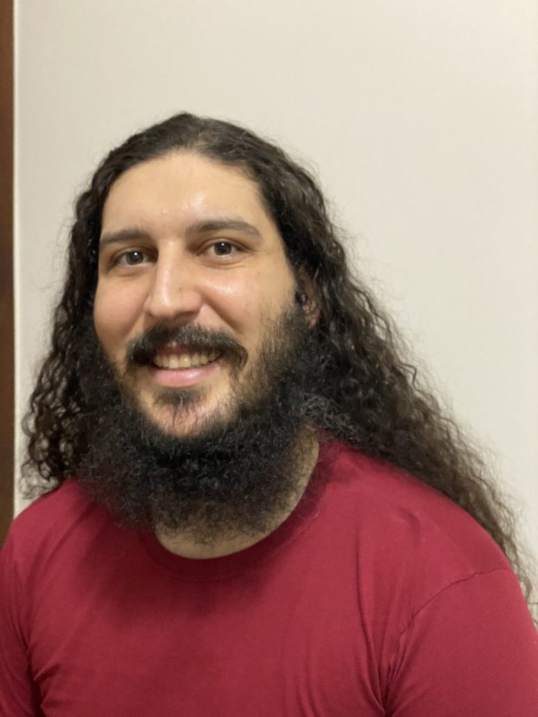 O psicólogo Renan, cabelos longos, olha para a câmera e sorri.