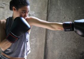 A imagem de uma mulher jovem com luvas de boxe, dando um soco, ilustra a luta quando se tem O “não” na maternidade atípica