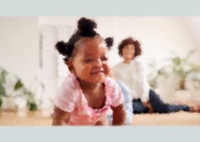 Foto de uma criança preta, 1 ano, desfocada, engatinhando. Ao fundo, sentada no tapete a mãe, também desfocada, observa. Acabei de receber o diagnóstico: meu filho é autista!