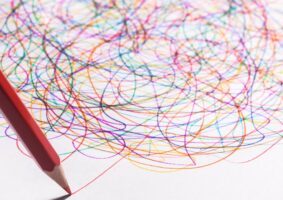 Neurodiversidade representada por um lápis de cor desenhando mais um risco num emaranhado de riscos coloridos