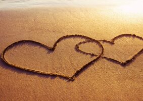 O desenho de dois corações entrelaçados, na areia da praia. Um maior, o outro menor.