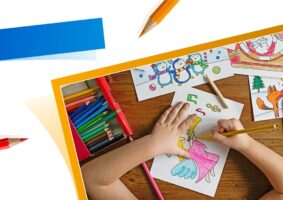 Mundo Inclusivo já: foto das mãos de uma criança desenhando sobre uma mesa, com vários desenhos espalhados, vista de cima.